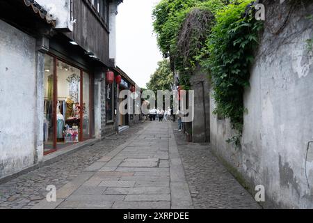 Suzhou, Chine - 11 juin 2024 : Une rue étroite et pavée dans une ville chinoise historique avec des bâtiments de chaque côté. Banque D'Images