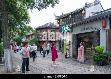 Suzhou, Chine - 11 juin 2024 : Une rue pavée bordée de bâtiments traditionnels chinois et de boutiques, avec des gens marchant dans la verdure. Banque D'Images