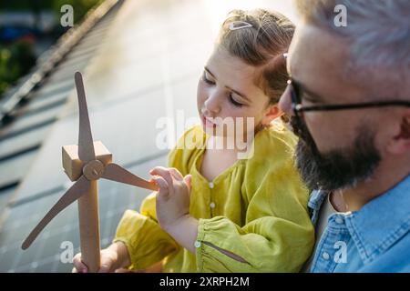 Fille et père sur le toit avec des panneaux solaires, tenant le modèle de l'éolienne. Installation solaire ou photovoltaïque sur le toit. Un avenir durable pour NEXT Banque D'Images