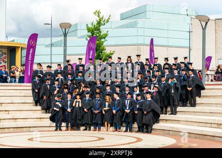 Groupe de diplômés en dehors de l'Université de Warwick après la cérémonie de remise des diplômes, posant sur quelques étapes se préparant à faire le lancer traditionnel de casquette. Banque D'Images