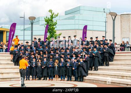 Groupe de diplômés en dehors de l'Université de Warwick après la cérémonie de remise des diplômes, posant sur quelques étapes se préparant à faire le lancer traditionnel de casquette. Banque D'Images