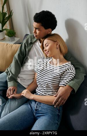 Un jeune couple interracial se détend sur un canapé dans leur appartement moderne, profitant d'un moment de calme ensemble. Banque D'Images