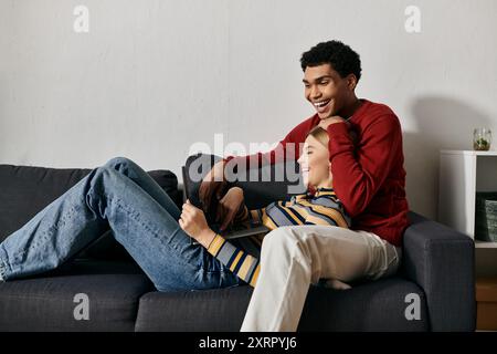 Un couple diversifié se lie joyeusement dans leur appartement élégant, riant et utilisant un ordinateur portable ensemble. Banque D'Images