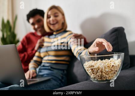 Un couple heureux et multiculturel se détend sur un canapé dans un appartement moderne, profitant d'une soirée cinéma ensemble. Banque D'Images