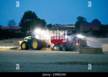 Les agriculteurs travaillent tard dans la nuit pour récolter la récolte début août. Les agriculteurs utilisent des lumières puissantes sur leurs tracteurs pour pouvoir récolter tard dans la soirée. La ferme est située dans le Warwickshire rural, dans les Midlands, Royaume-Uni. Banque D'Images