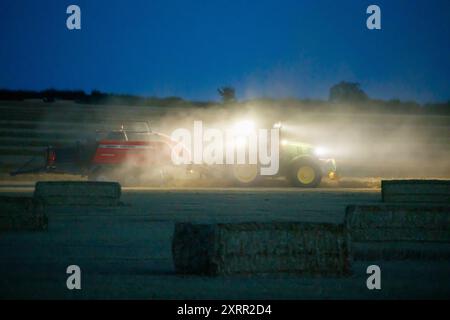 Les agriculteurs travaillent tard dans la nuit pour récolter la récolte début août. Les agriculteurs utilisent des lumières puissantes sur leurs tracteurs pour pouvoir récolter tard dans la soirée. La ferme est située dans le Warwickshire rural, dans les Midlands, Royaume-Uni. Banque D'Images