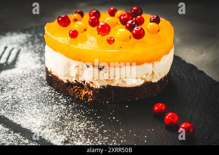 Un gâteau ou un dessert à base de gelée de mangue ou d'argousier, recouvert de crème au fromage cottage et de biscuits au chocolat, décoré d'airelles et de poudre Banque D'Images