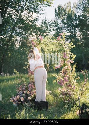 Femme arrangeant des fleurs sur une arche dans un cadre extérieur ensoleillé Banque D'Images