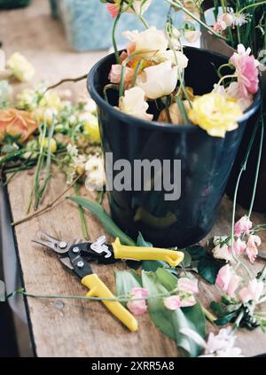 Seau de fleurs assorties et sécateurs jaunes sur une table en bois Banque D'Images