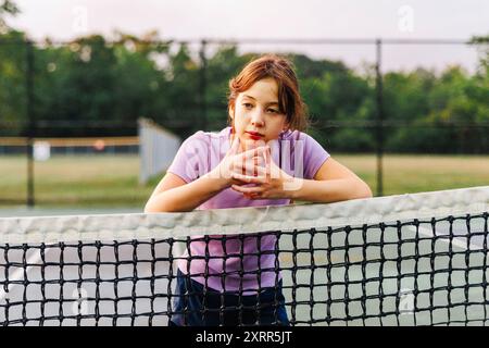 Portrait d'une fille réfléchie penchée sur le filet au court de tennis Banque D'Images