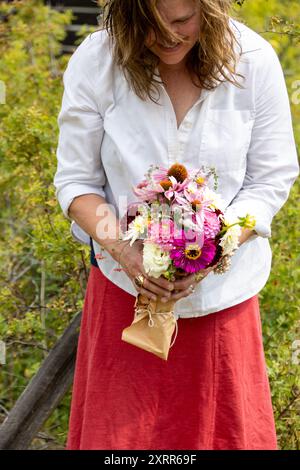 Femme tenant un bouquet de fleurs colorées tout en souriant à l'extérieur Banque D'Images