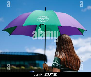 Fille aux cheveux longs tenant un parapluie pour garder le soleil hors joueur aux championnats de Wimbledon 2024, Londres, Angleterre. Banque D'Images