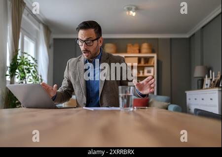 Inquiet jeune entrepreneur masculin regardant ordinateur portable en état de choc tout en travaillant au bureau dans le bureau à domicile Banque D'Images