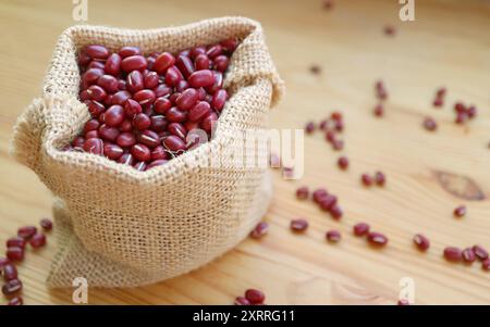 Gros plan de haricots rouges Adzuki séchés dans un sac en toile de jute isolé sur une table en bois Banque D'Images