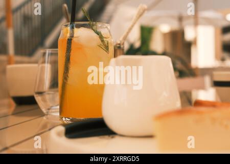 Un verre de jus d'orange avec une paille est assis sur une table à côté d'une tasse blanche. Concentrez-vous sur le jus d'orange. Banque D'Images