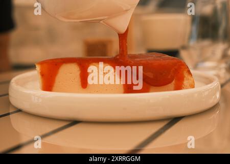 Une tranche de cheesecake avec une sauce fraise arrosée sur le dessus. Le cheesecake est servi sur une assiette blanche et placé sur une table en bois Banque D'Images