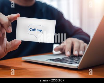 Appelez-moi concept. Texte « APPELEZ-MOI » sur la carte blanche de nom d'entreprise montrant par la main d'homme d'affaires, qui travaille avec un ordinateur portable sur le lieu de travail. nam horizontal Banque D'Images