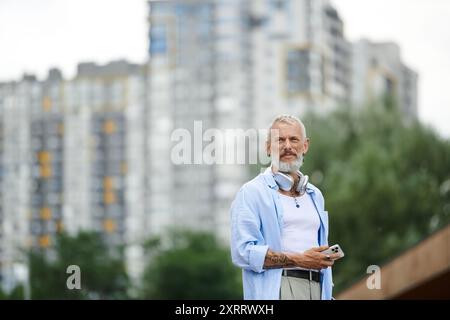 Un homme mûr avec des tatouages et une barbe grise debout dans un cadre urbain. Banque D'Images