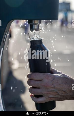 Une main tenant une bouteille d'eau et la remplissant à partir d'une fontaine d'eau extérieure, avec une faible profondeur de champ Banque D'Images