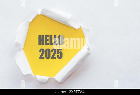 Une note jaune avec HELLO 2025 JETTE un coup d'œil à travers un livre blanc déchiré, symbolisant un nouveau départ et des opportunités commerciales pour l'année à venir. Banque D'Images