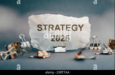 Un morceau de papier déchiré affiche le mot Stratégie le long de l'année 2025, entouré de pinces de reliure métalliques, symbolisant la planification d'entreprise. Banque D'Images