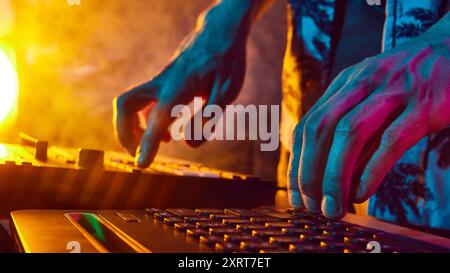 Les mains du DJ ajustent les commandes, baignées d'une douce lueur de lumières colorées, prêtes à enflammer la piste de danse avec des rythmes électrisants. Banque D'Images