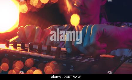 Les mains du DJ dansent à travers la table de mixage, éclairées par des néons chauds, créant une bande-son pleine d'énergie et de rythme pour la nuit. Banque D'Images