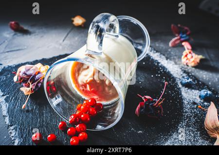 Portion originale de la panna cotta dessert avec des airelles, des myrtilles dans un verre couché sur un tableau noir avec des fleurs séchées. Design alimentaire, photo f Banque D'Images