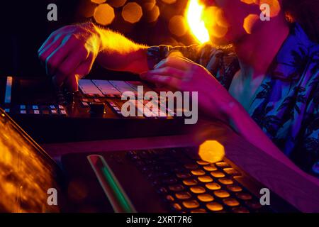 Mixeur de travail des mains de DJ, baigné dans la lueur ambiante des lumières de scène, façonnant le rythme qui va déplacer la foule. Banque D'Images