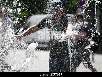 12 août 2024, Hesse, Francfort-sur-le-main : par temps chaud en été, un homme se rafraîchit dans les fontaines d'eau de Rathenauplatz dans le centre-ville. Photo : Arne Dedert/dpa Banque D'Images