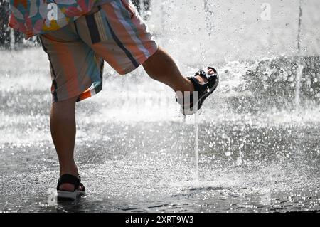 12 août 2024, Hesse, Francfort-sur-le-main : par temps chaud en été, un homme se rafraîchit les pieds dans les fontaines d'eau de Rathenauplatz dans le centre-ville. Photo : Arne Dedert/dpa Banque D'Images