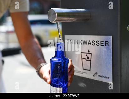 12 août 2024, Hesse, Francfort-sur-le-main : par temps chaud en été, un chauffeur de taxi remplit sa bouteille d'eau à la fontaine d'eau potable de Paulsplatz. Photo : Arne Dedert/dpa Banque D'Images