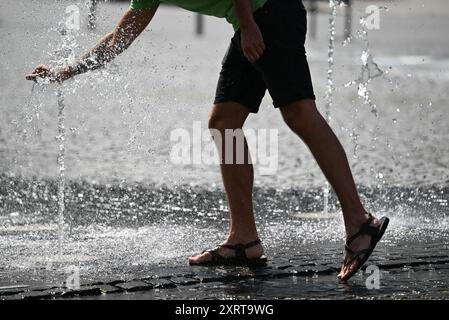 12 août 2024, Hesse, Francfort-sur-le-main : par temps chaud en été, un homme se rafraîchit dans les fontaines d'eau de Rathenauplatz dans le centre-ville. Photo : Arne Dedert/dpa Banque D'Images