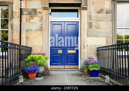 Charmante porte bleue d'un bâtiment historique en pierre orné de plantes en pot. Banque D'Images