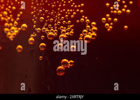 Vue rapprochée des bulles d'air de couleur goden scintillent dans un verre d'eau de cola glacée. Banque D'Images