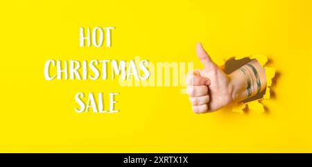 Une main donnant un pouce vers le haut avec les mots Hot Christmas Sale écrit ci-dessous. L'image a une ambiance positive et festive, encourageant les gens à acheter du Banque D'Images