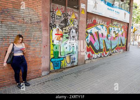 Barcelona Spain,Catalonia Catalunya,Carrer de nouveaux Antoni Maria Claret,Horta-Guinardo,Street scene,femme fumant,debout contre le mur,lecture regardant, Banque D'Images
