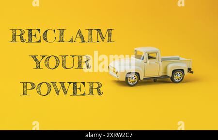 Un camion-jouet est sur un fond jaune avec les mots Reclaim Your Power écrits en dessous Banque D'Images