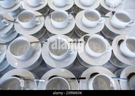 Regardant vers le bas sur une table pleine de tasses blanches et soucoupes avec des cuillères prêtes à être remplies de boissons chaudes, thé, café, etc Banque D'Images