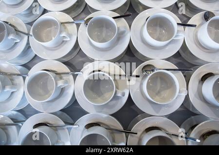 Regardant vers le bas sur une table pleine de tasses blanches et soucoupes avec des cuillères prêtes à être remplies de boissons chaudes, thé, café, etc Banque D'Images