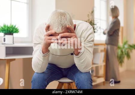 Malheureux vieil homme âgé assis sur la chaise couvrant le visage avec les mains se querellant femme à la maison. Banque D'Images