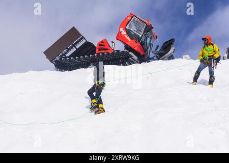 Elbrus, Russie - 01 août 2024 : les grimpeurs pratiquent leurs compétences d'escalade sur une pente enneigée avec des chats à neige en arrière-plan Banque D'Images