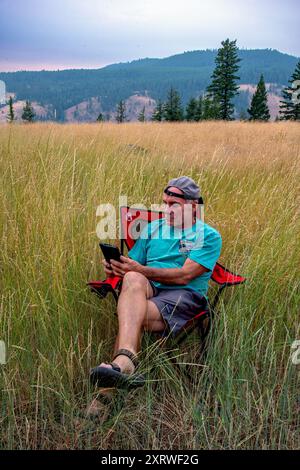 Adulte célibataire retraité masculin se détend après une journée d'escalade et lit un livre sur son Kindle. Blue Mountains, Oregon Banque D'Images