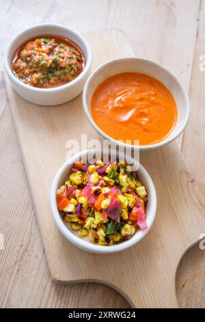 Trois petits bols blancs sur une planche de bois recouverte d'une soupe mexicaine fraîchement préparée, sauce piquante et salade de maïs doux et d'oignons. Banque D'Images