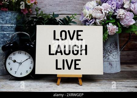 Love Laugh Live texte écrit sur carte papier avec réveil et décoration de fleurs sur fond en bois Banque D'Images