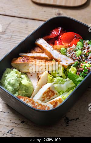 Une boîte à lunch en plastique avec trempette à l'avocat, salade ffresh, haloumi grillé et lanières de poulet. Banque D'Images