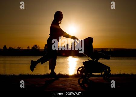 Silhouette d'une mère tirant une poussette contre le coucher du soleil près du lac Banque D'Images