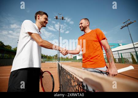 Poignée de main de respect. Deux hommes, joueurs de tennis professionnels échangeant des gestes respectueux après un bon match intensif sur terrain de terre battue extérieur. Banque D'Images