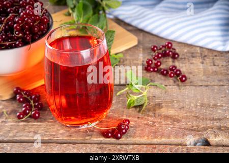 Jus de cassis rouge ou liqueur dans le verre, sur fond de table en bois, avec menthe et espace de copie de baies de cassis fraîches Banque D'Images