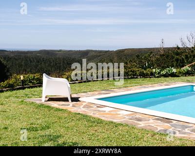 Un cadre serein au bord de la piscine avec des chaises longues blanches donnant sur une vue panoramique sur les montagnes luxuriantes sous un vaste ciel Banque D'Images